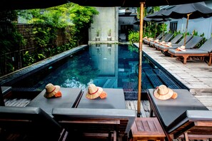A poolside area with lounge chairs and umbrellas, a concrete wall with plants, and a clear pool.