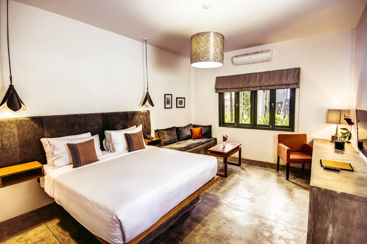 Une chambre d’hôtel avec un grand lit, un canapé, un bureau et une fenêtre donnant sur un paysage verdoyant.