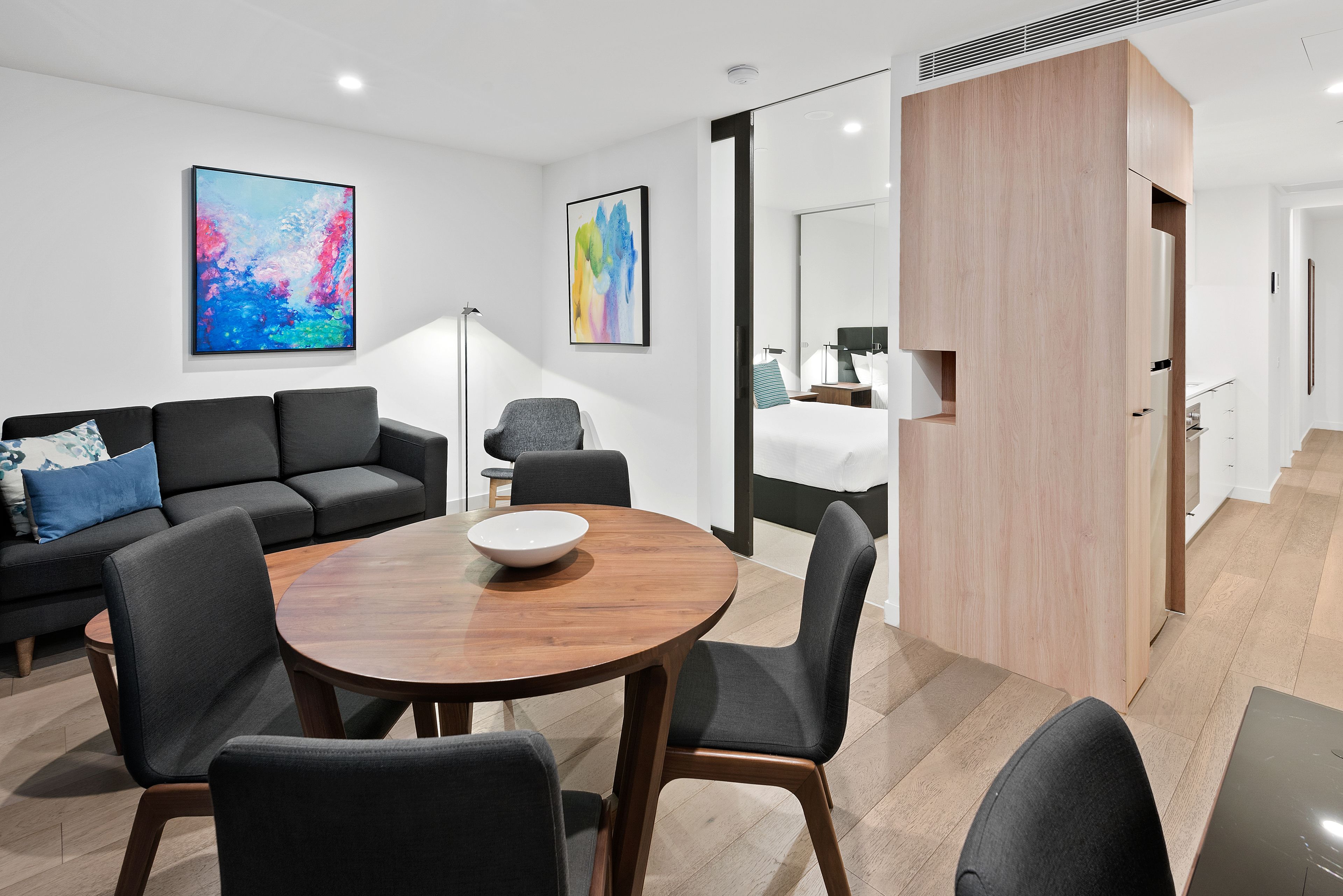 A modern hotel room with a dining area, a sofa, a bed, and a large mirror.