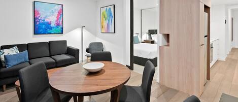 A modern hotel room with a dining area, a sofa, a bed, and a large mirror.