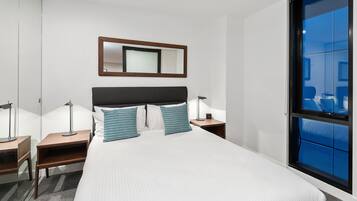 A modern hotel room with a large bed, bedside tables, a mirror, and a window with a view.