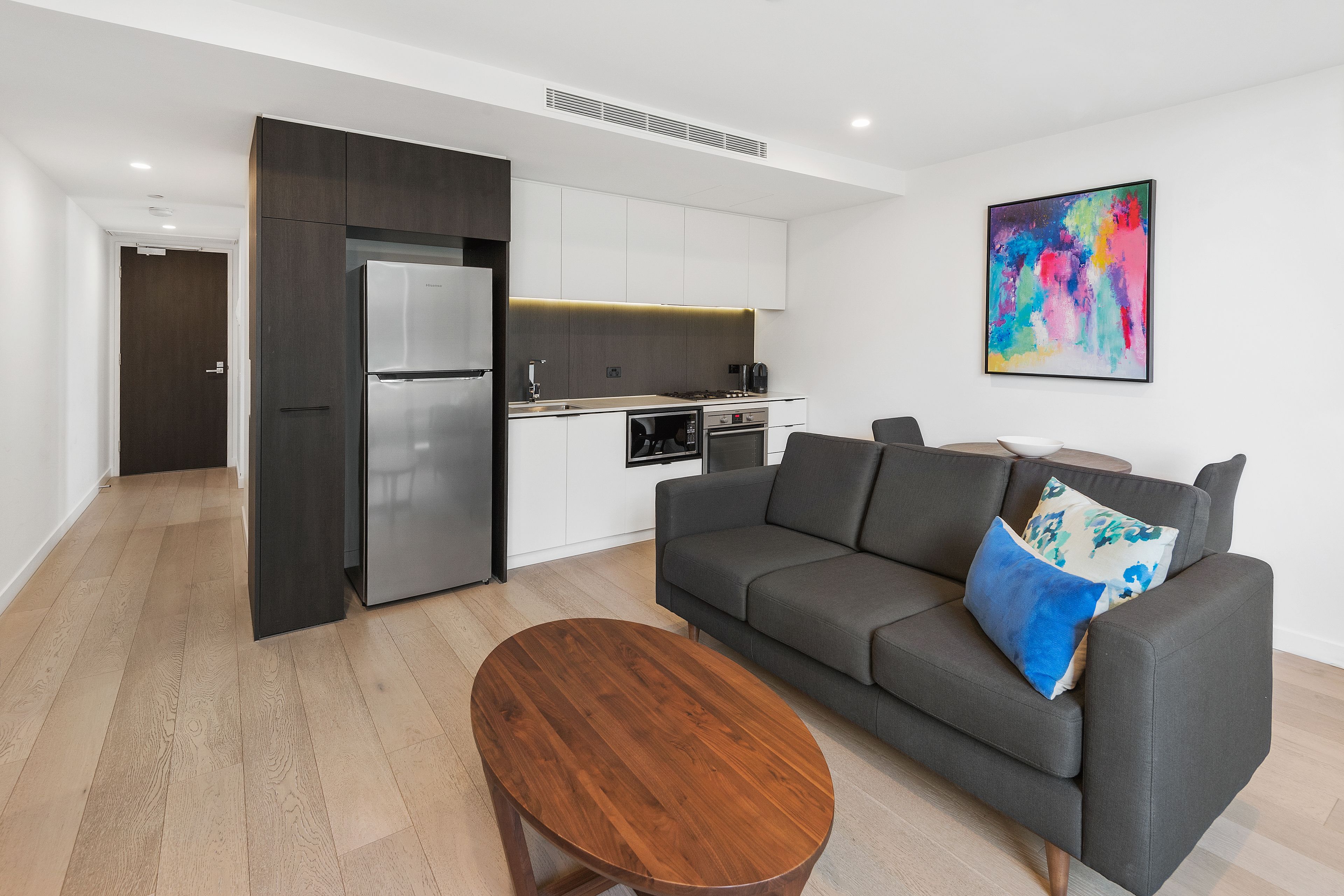 A modern living room with a grey sofa, a wooden coffee table, and a kitchen in the background.