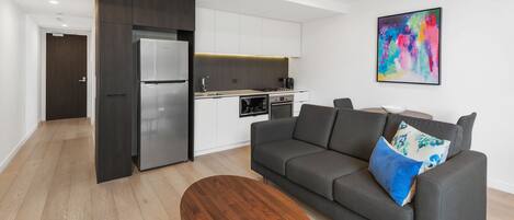 A modern living room with a grey sofa, a wooden coffee table, and a kitchen in the background.