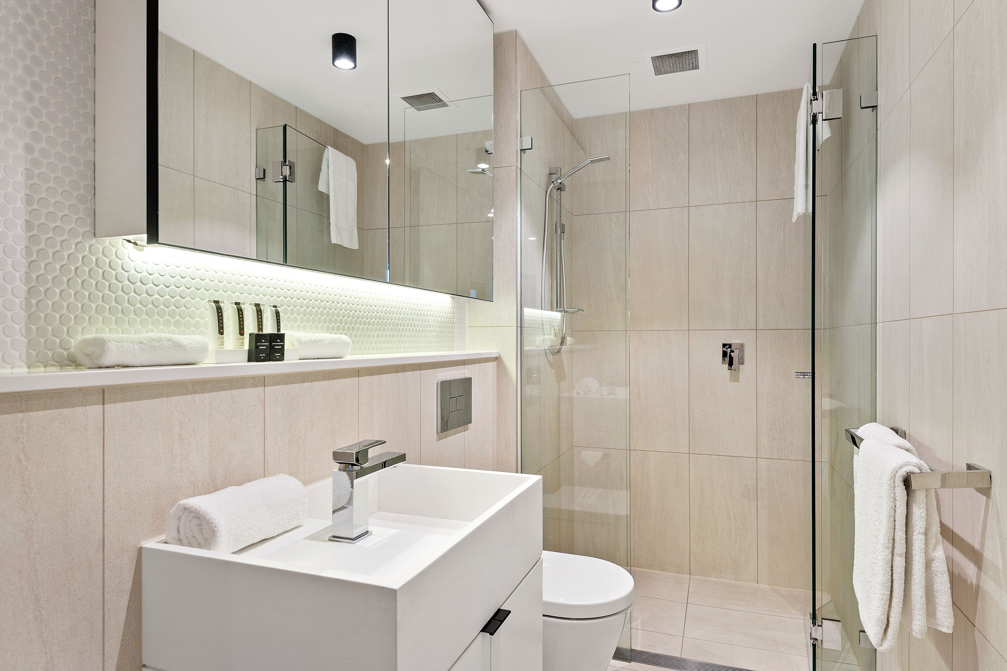 A modern bathroom with a glass-enclosed shower, a white sink, and a large mirror.