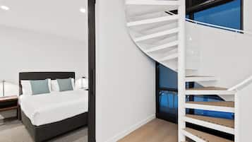 A modern bedroom with a curved staircase, a bed with white bedding, and a nightstand with a lamp.