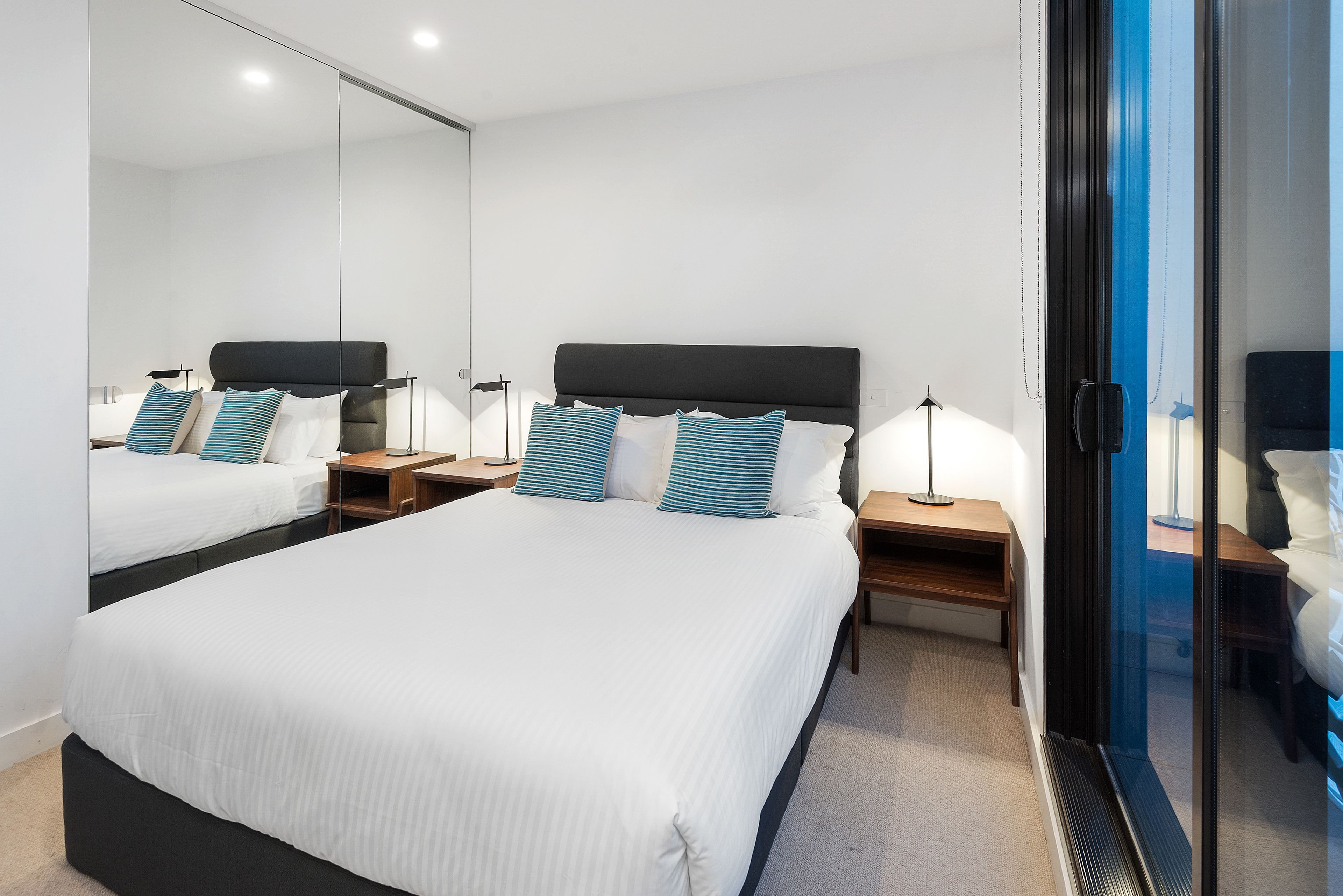 Una habitación de hotel moderna con una cama grande, dos mesitas de noche con lámparas y un espejo amplio.