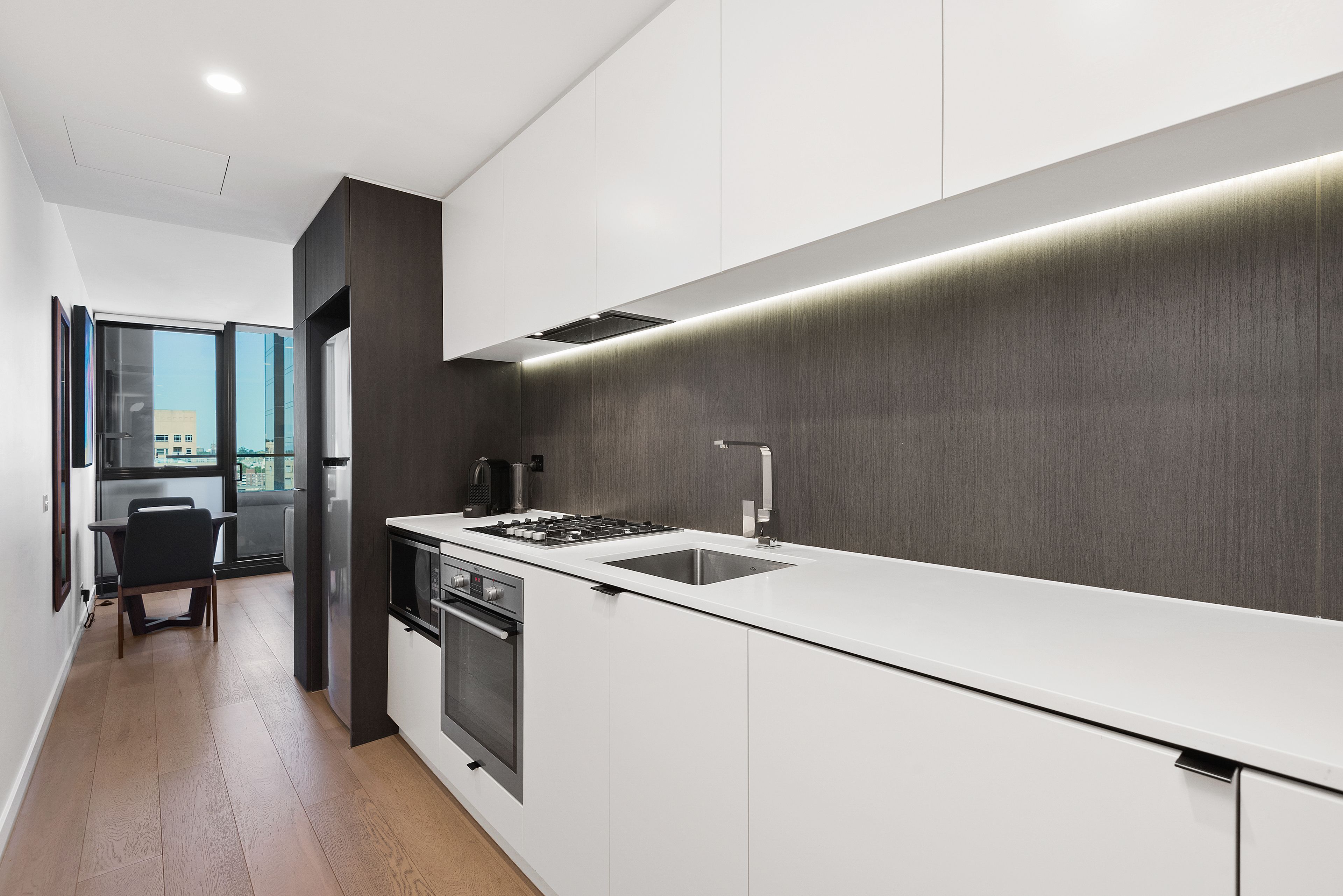 A modern kitchen with white cabinetry, a stainless steel sink, and a built-in oven.