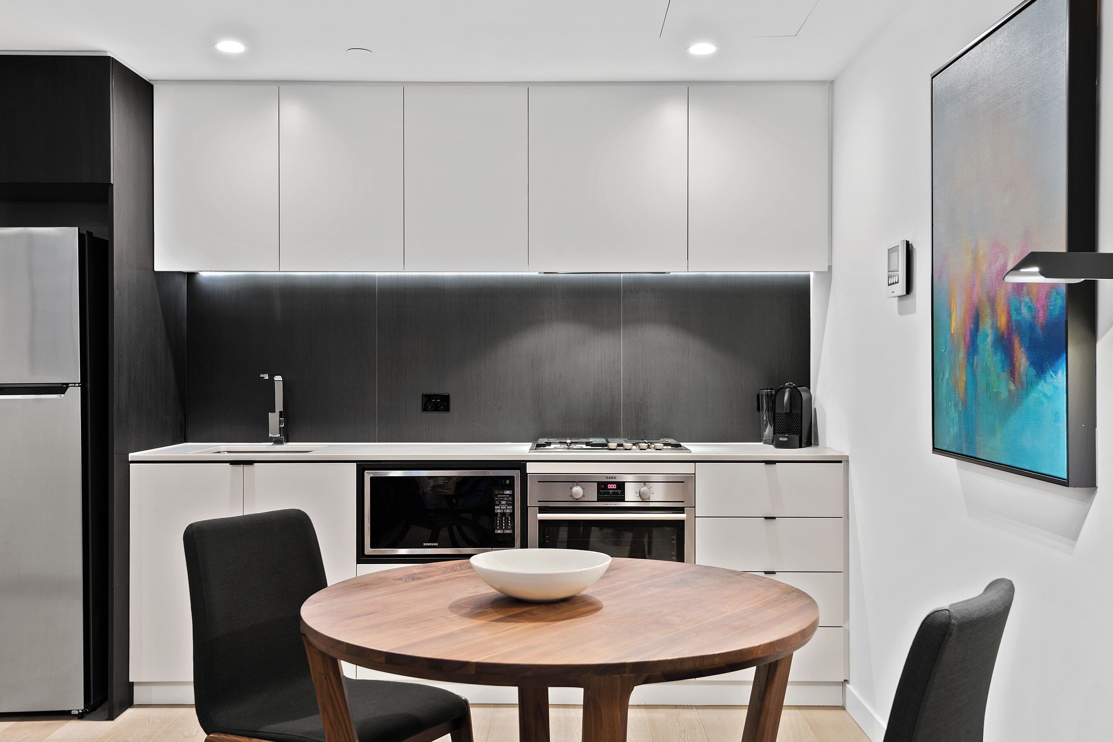 Una cocina moderna con armarios blancos, una mesa de comedor de madera y un cuadro abstracto colorido en la pared.