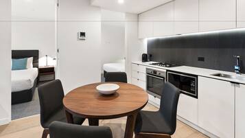 A modern kitchen with white cabinets, a black countertop, and a built-in oven. There is a dining area with a wooden table and four chairs.