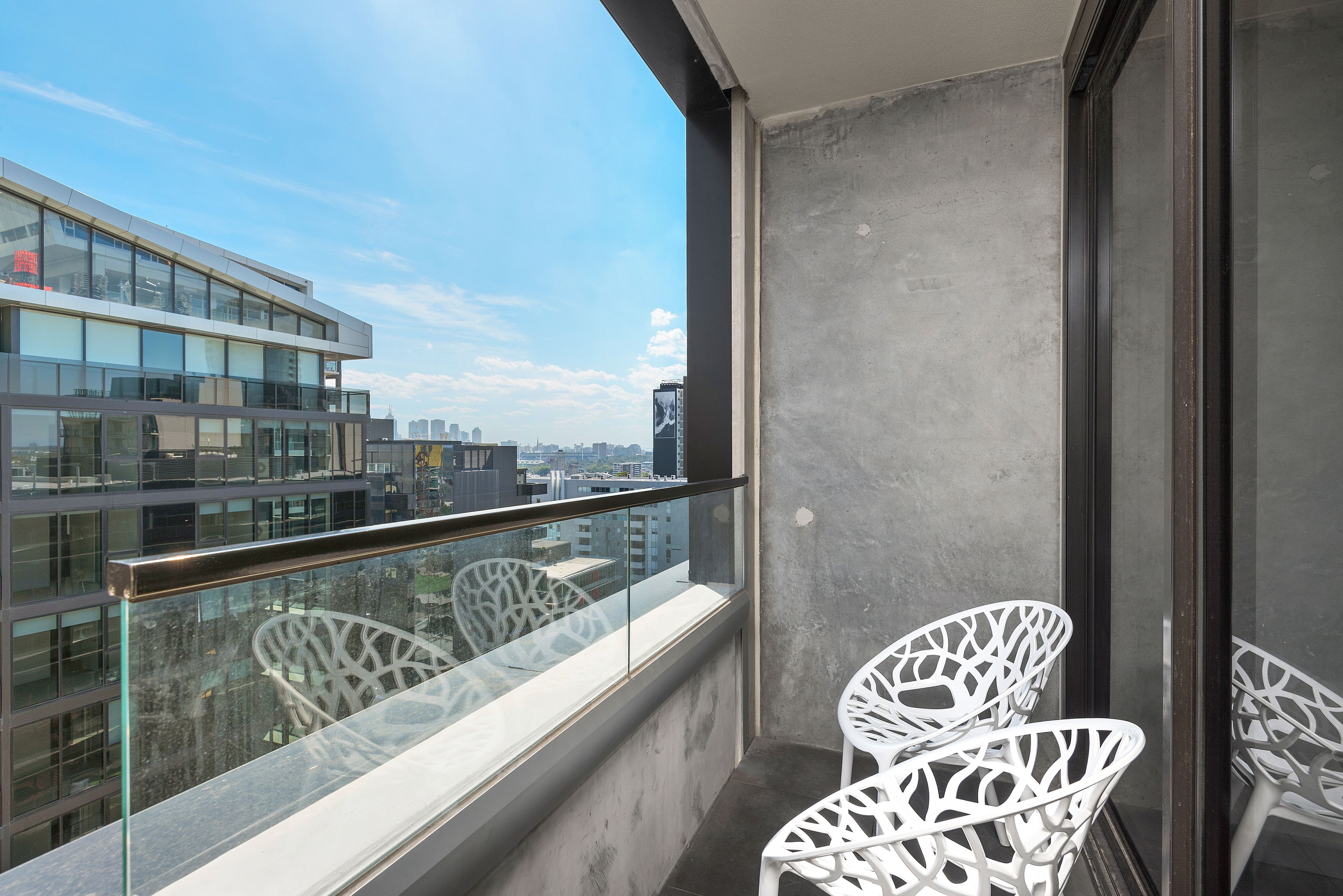 Ein Balkon mit Glasgeländer, weißen Stühlen und Blick auf die Stadt.