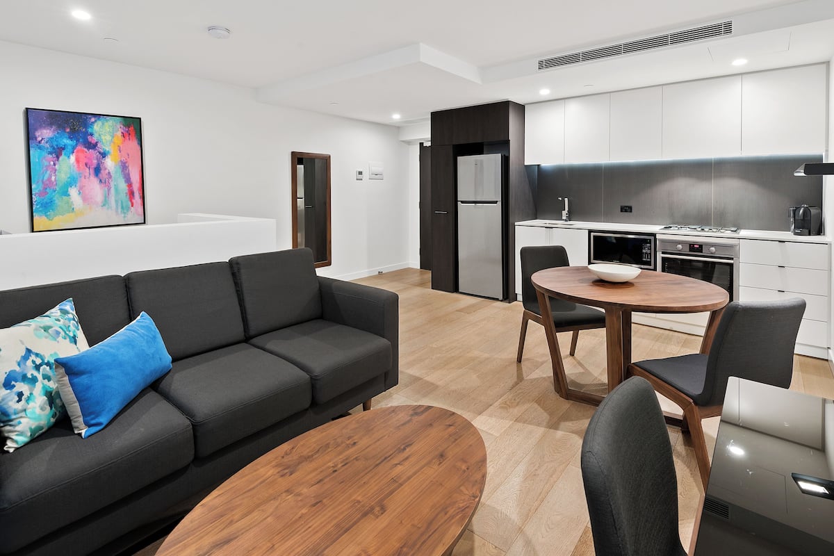 A modern living room with a black sofa, a wooden coffee table, and a dining area with a round table and chairs.