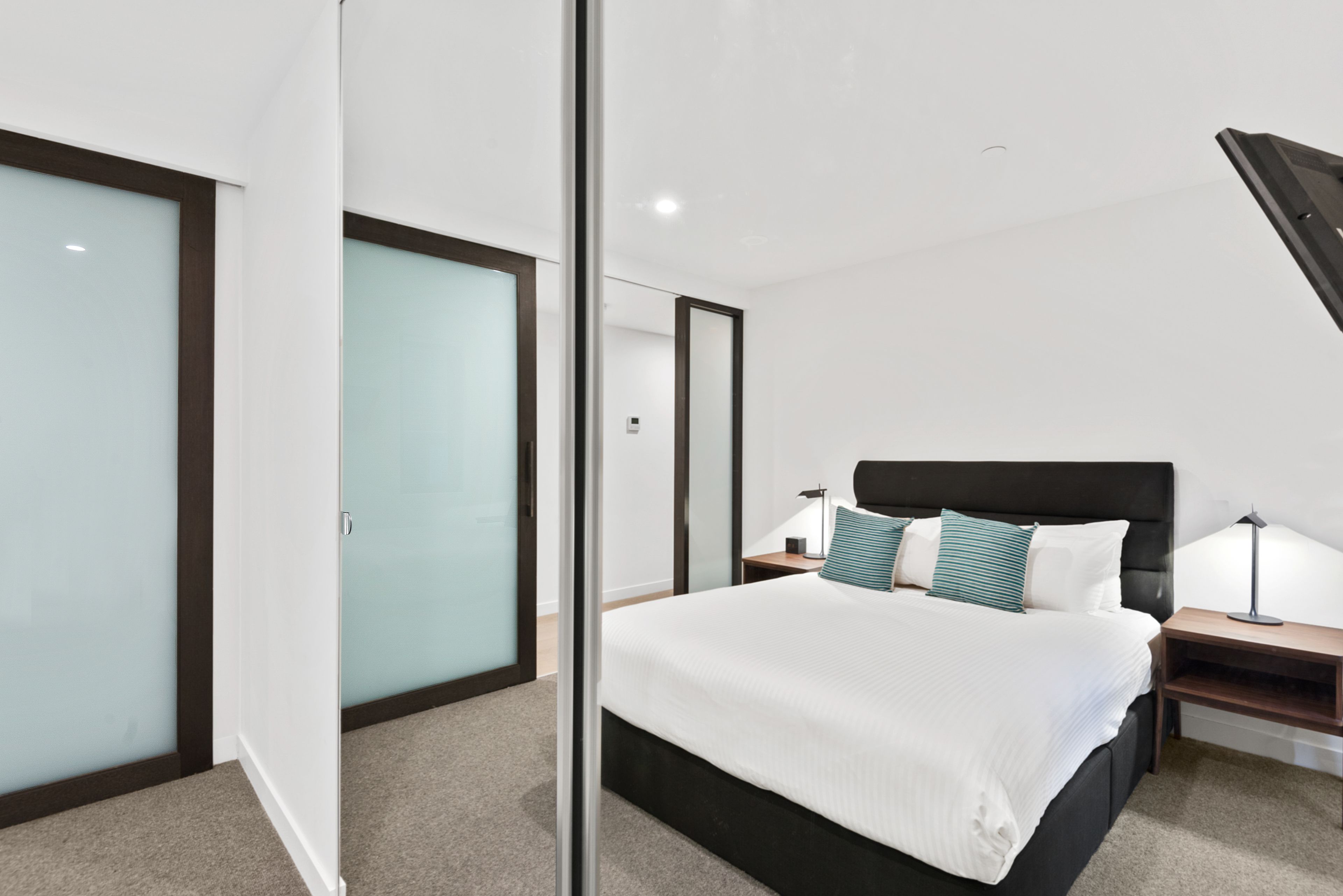 A modern hotel room with a large bed, a nightstand, a lamp, and a sliding door.