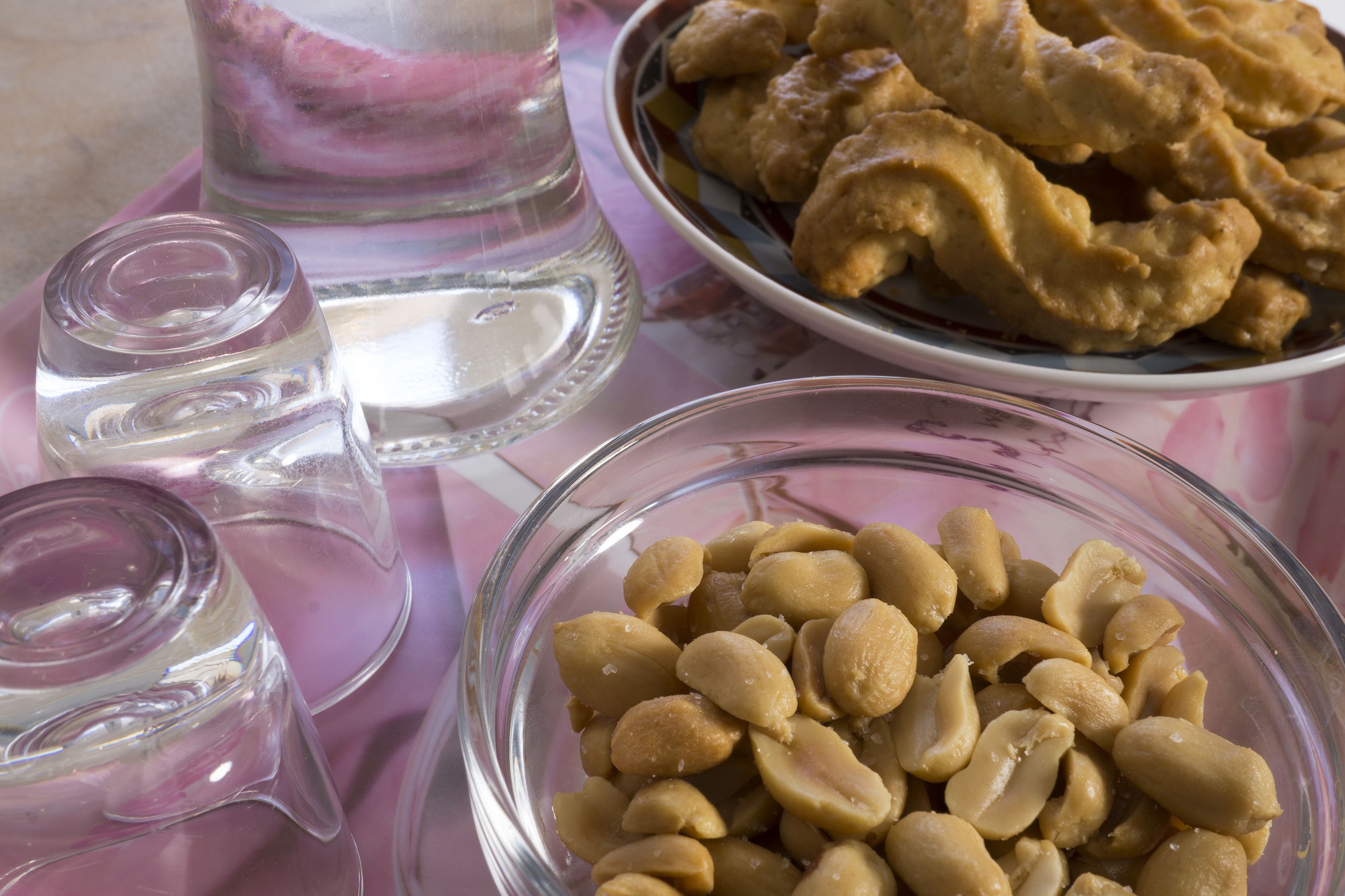 Een tafel met een glazen schaal vol pinda's, een bord met gefrituurde snacks en twee glaasjes water.