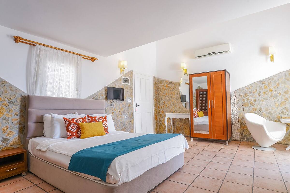A bedroom with a bed, bedside tables, a wardrobe, a mirror, a TV, and a bathroom with a bathtub and a chair.