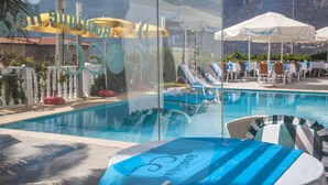 A pool area with lounge chairs and umbrellas, a glass wall reflecting the pool and mountains, and a sign with the hotel's name. - Peace Hotel (Kas)