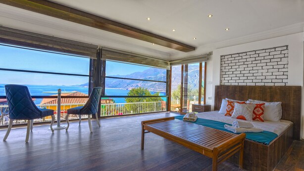 A hotel room with a large balcony, wooden flooring, a bed with pillows, and a view of the sea and mountains. - Peace Hotel (Kas)