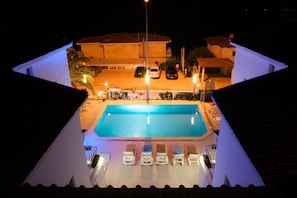 A swimming pool with lounge chairs, a covered parking area, and buildings in the background. - Peace Hotel (Kas)