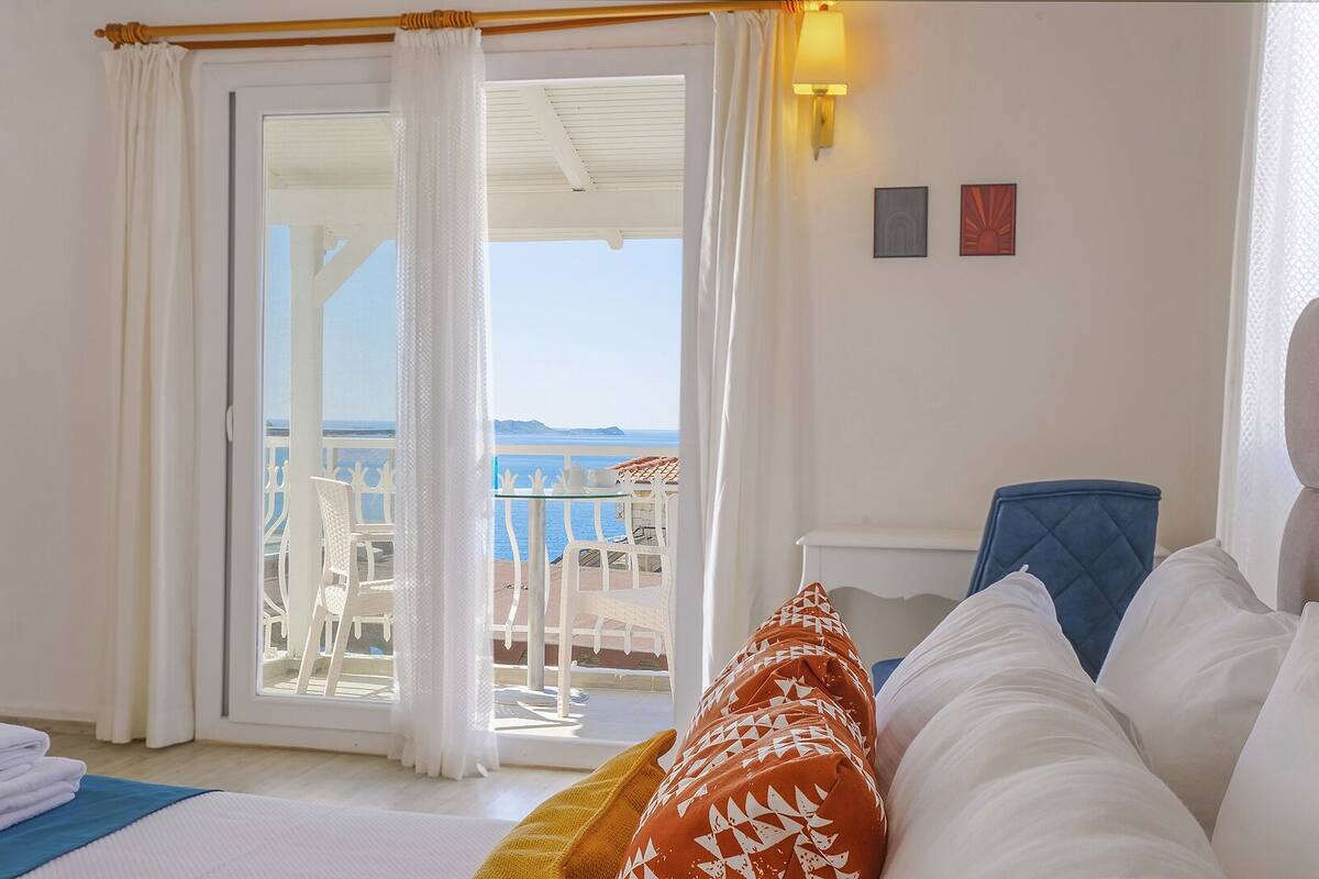 A hotel room with a balcony, white furniture, and a view of the sea.