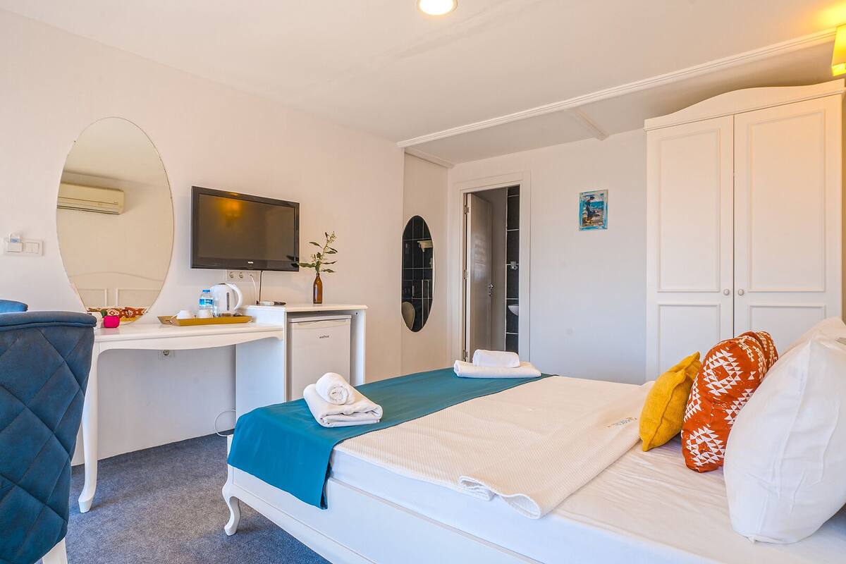 A hotel room with a bed, a desk, a chair, a TV, and a wardrobe.