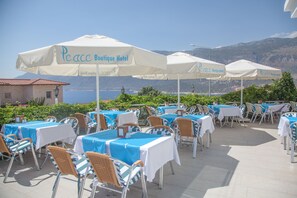 Outdoor seating with tables and chairs, covered by umbrellas, and a view of the sea and mountains in the background. - Peace Hotel (Kas)