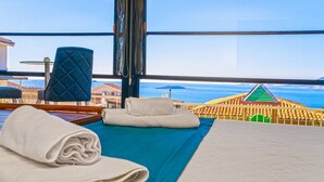 A hotel room with a bed, a blue quilted chair, and a view of the sea and buildings. - Peace Hotel (Kas)