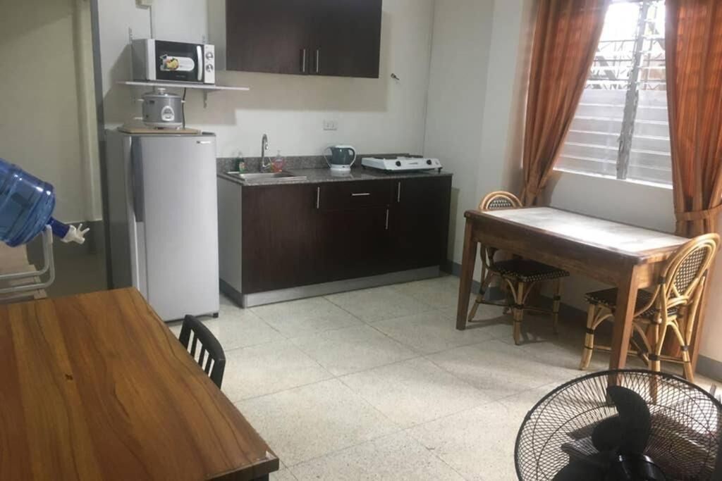 Une cuisine compacte équipée d’un four à micro-ondes, d’une cuisinière et d’un évier. On y trouve une table à manger avec des chaises, ainsi qu’une fenêtre avec des rideaux.