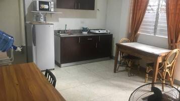 Une cuisine compacte équipée d’un four à micro-ondes, d’une cuisinière et d’un évier. On y trouve une table à manger avec des chaises, ainsi qu’une fenêtre avec des rideaux.