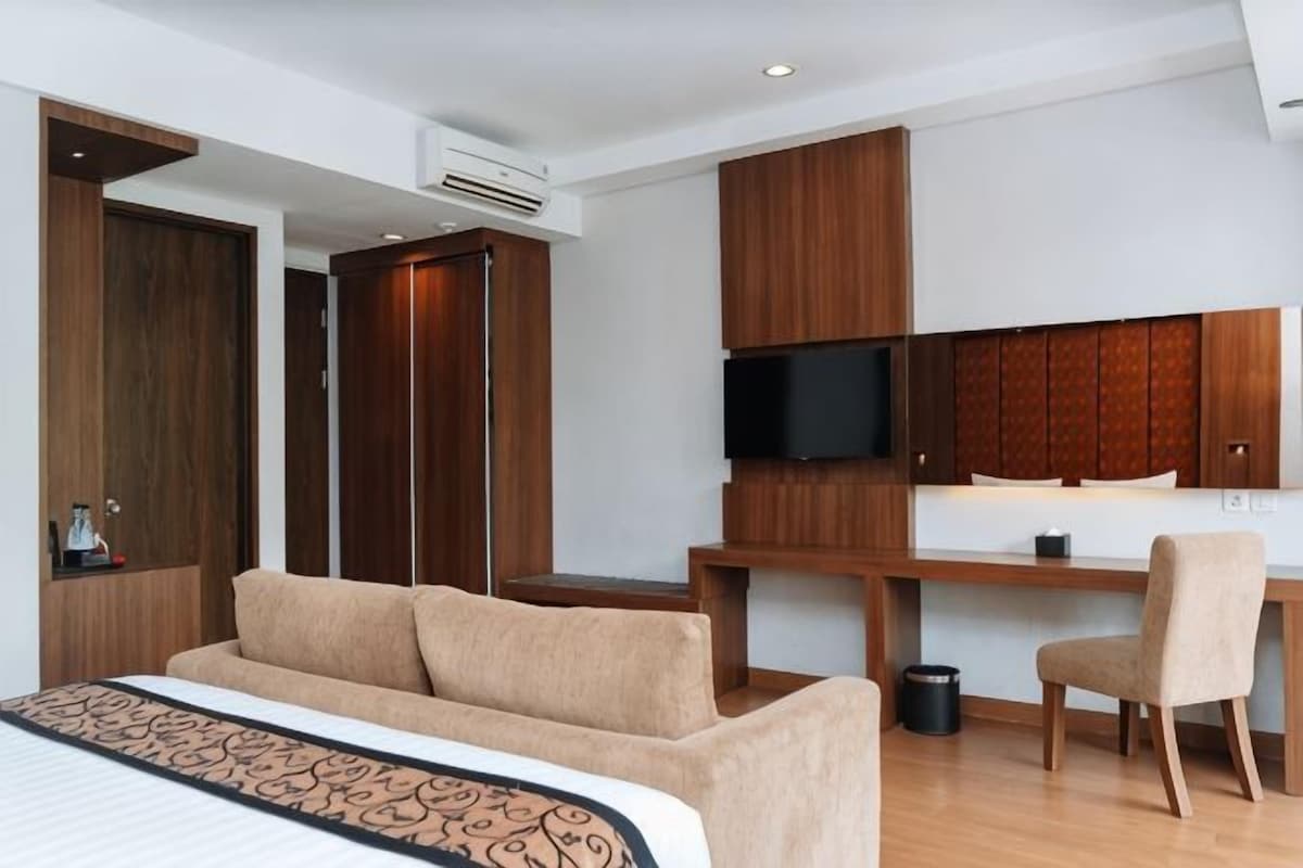 A hotel room with a bed, a desk, a chair, a television, and built-in wardrobes.