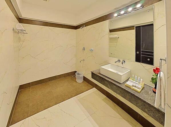 A modern bathroom with a marble vanity, a large mirror, a bathtub, and a shower. - Poppys Hotel (Madurai)