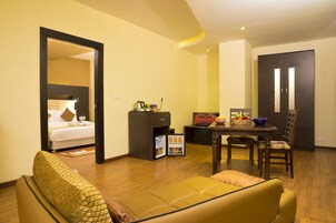 Une chambre d’hôtel comprenant un lit, un canapé, une table à manger avec des chaises, un petit coin cuisine et une porte donnant sur une autre pièce.