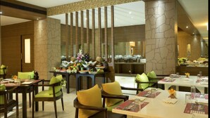 A restaurant with a modern interior, featuring a central dining area with tables and chairs, and a decorative wall with a crack pattern. - Poppys Hotel (Madurai)