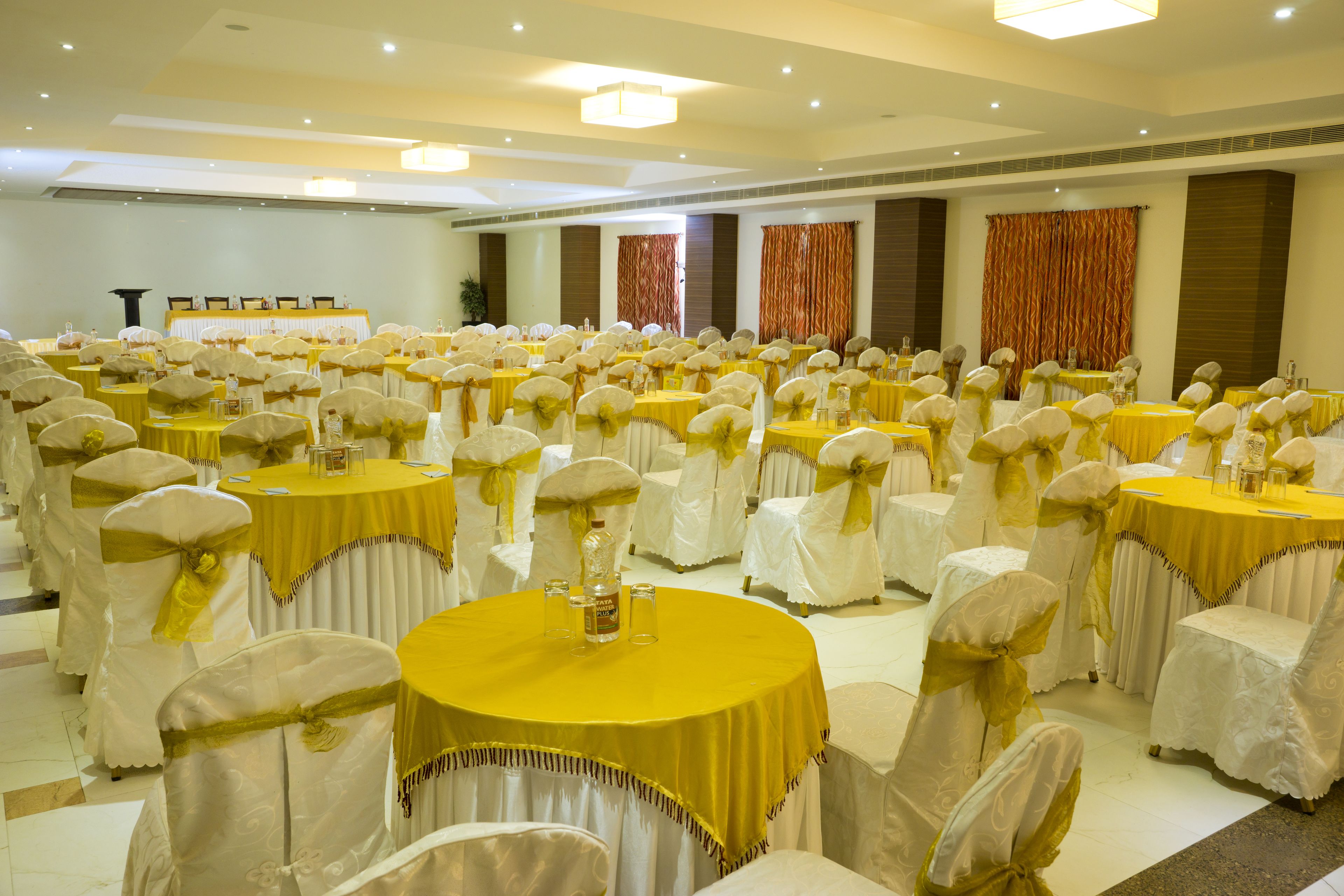 A banquet hall with round tables covered in yellow tablecloths and white chairs with gold sashes.