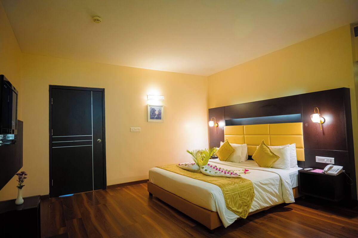 Een hotelkamer met een bed, nachtkastje, lamp en een deur.