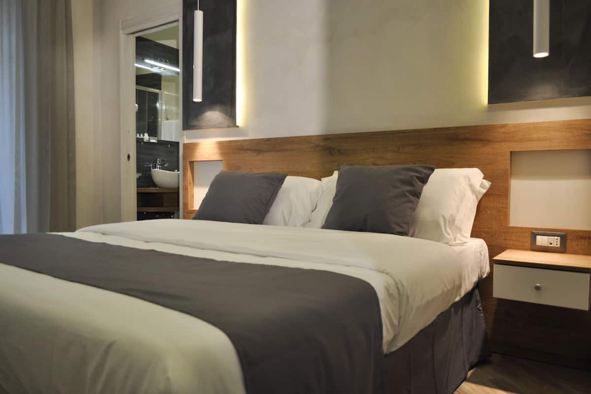 A modern hotel room with a large bed, a wooden headboard, a nightstand, and a built-in closet with a vanity.
