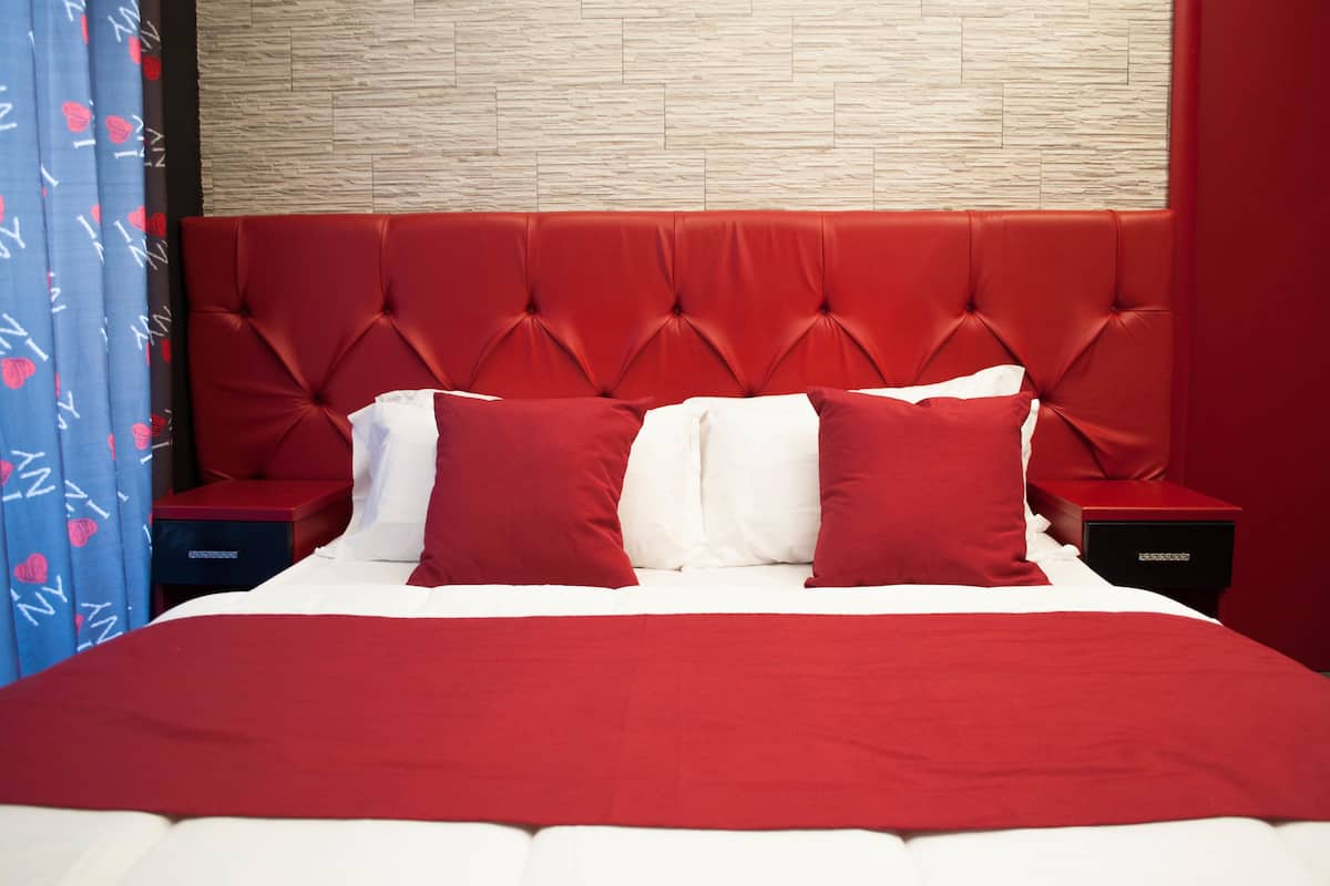 A bed with a red headboard and white bedding, flanked by red nightstands and a blue curtain with a heart pattern.