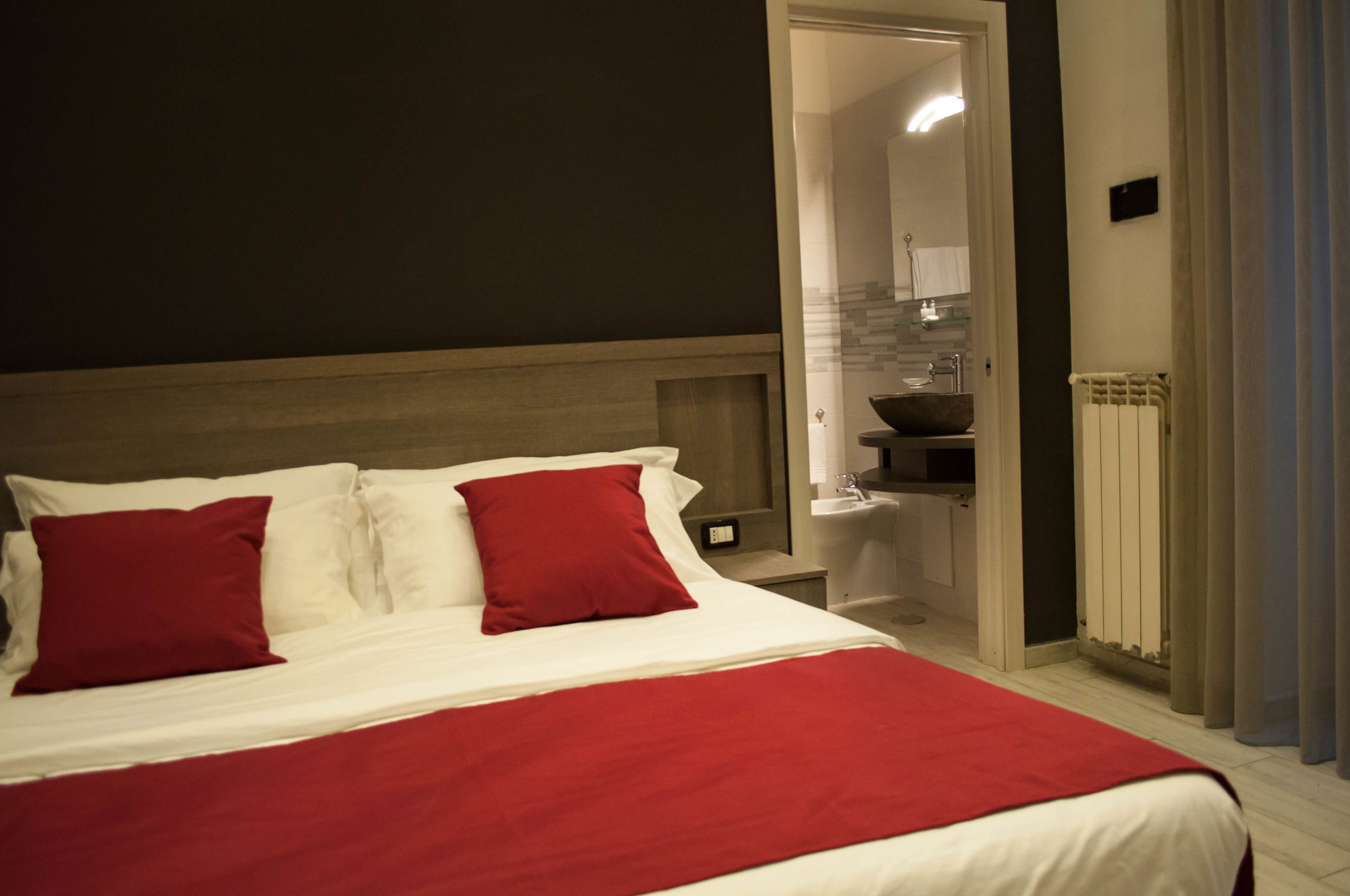 Ein Hotelzimmer mit Bett, Nachttisch, roter Decke und einem durchgegangenen Tür sichtbaren Badezimmer.
