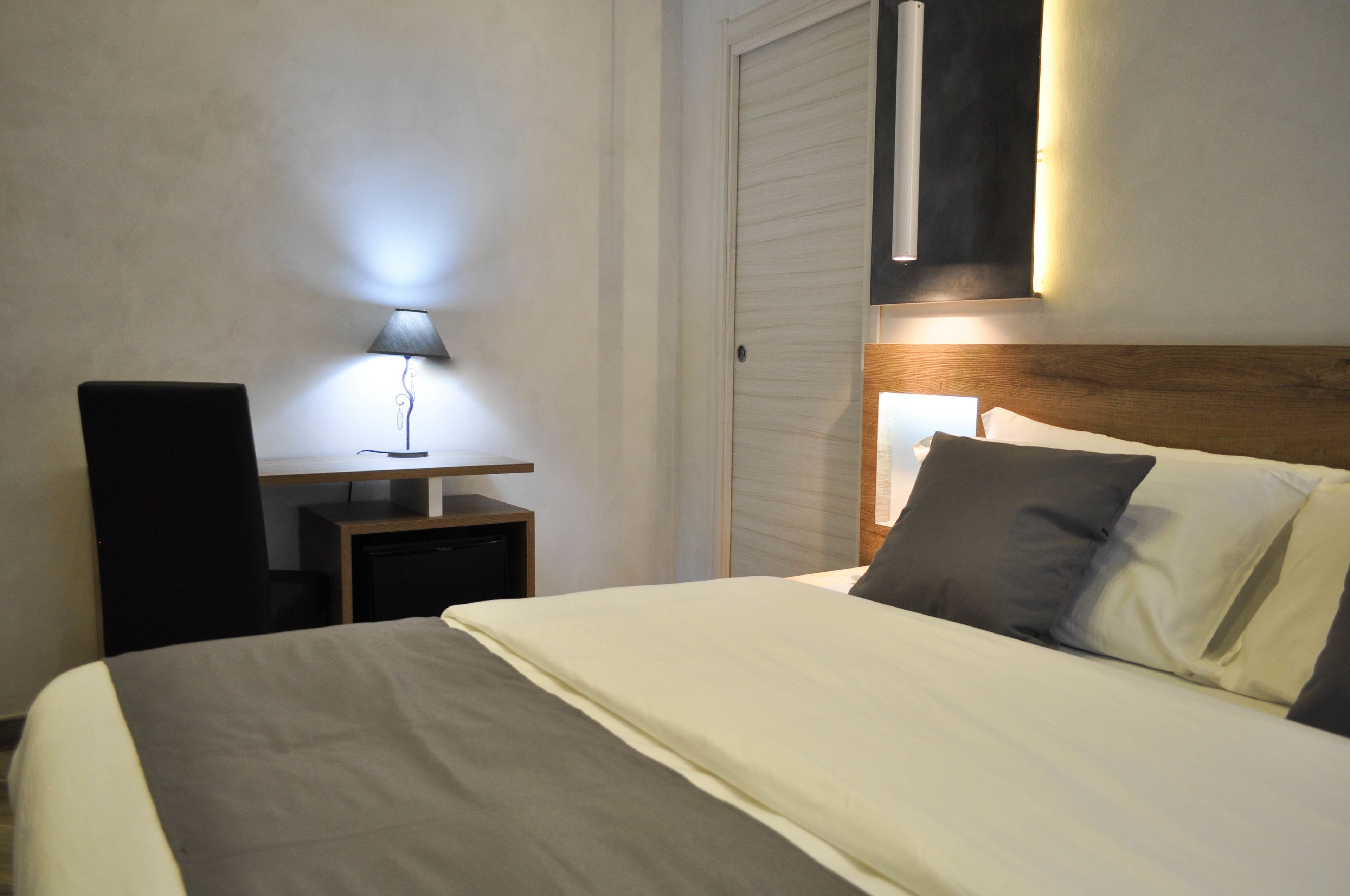 Une chambre d’hôtel bien rangée, avec un lit, une table de chevet, une lampe et une tête de lit dotée d’un luminaire.
