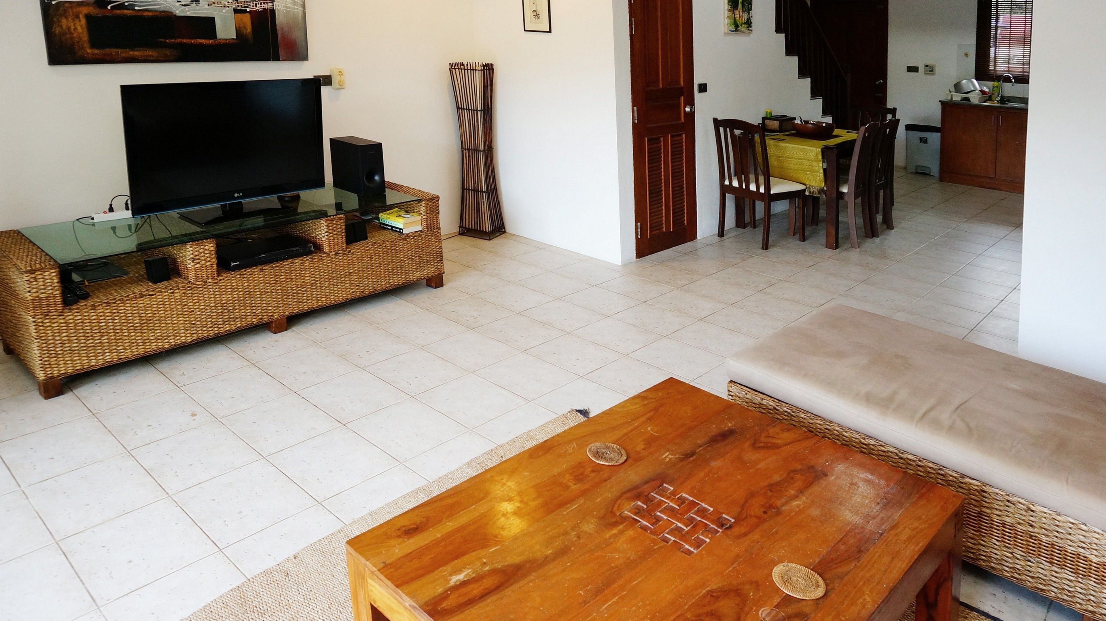 A living room with a TV, wicker furniture, a dining area with a yellow tablecloth, and a staircase leading upstairs.