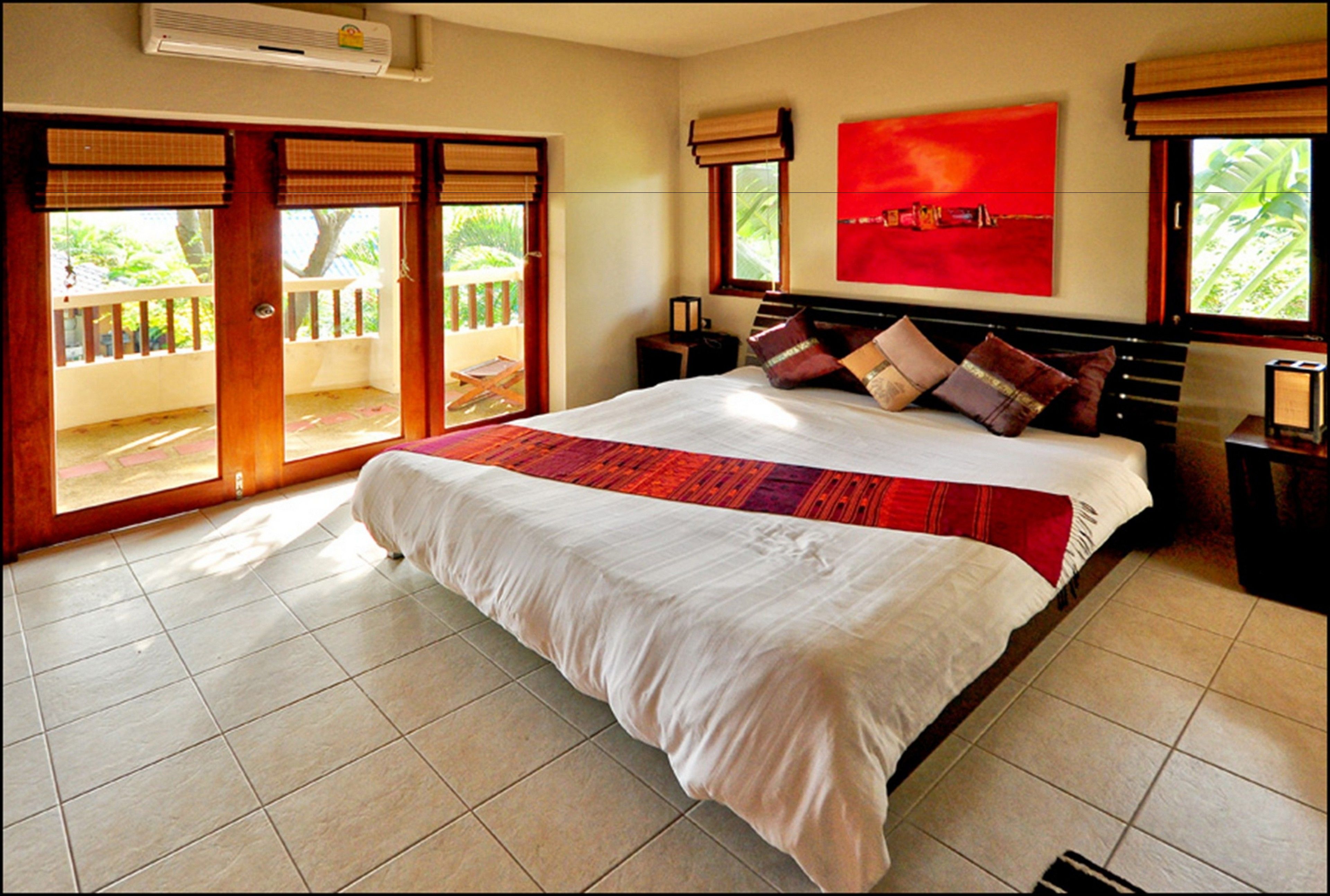 A bedroom with a large bed, a red abstract painting, and a view of a balcony with a wooden railing.