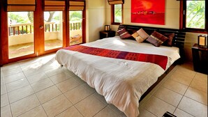 A bedroom with a large bed, a red abstract painting, and a view of a balcony with a wooden railing.