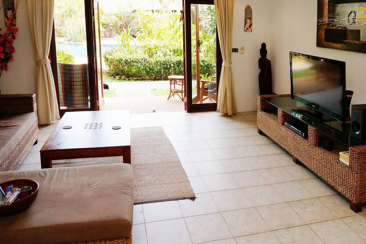 Una sala de estar con sofá, mesa de centro, televisor y mueble de entretenimiento de mimbre.