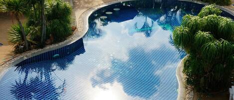 A large, curved swimming pool surrounded by palm trees and a patio area with outdoor seating.
