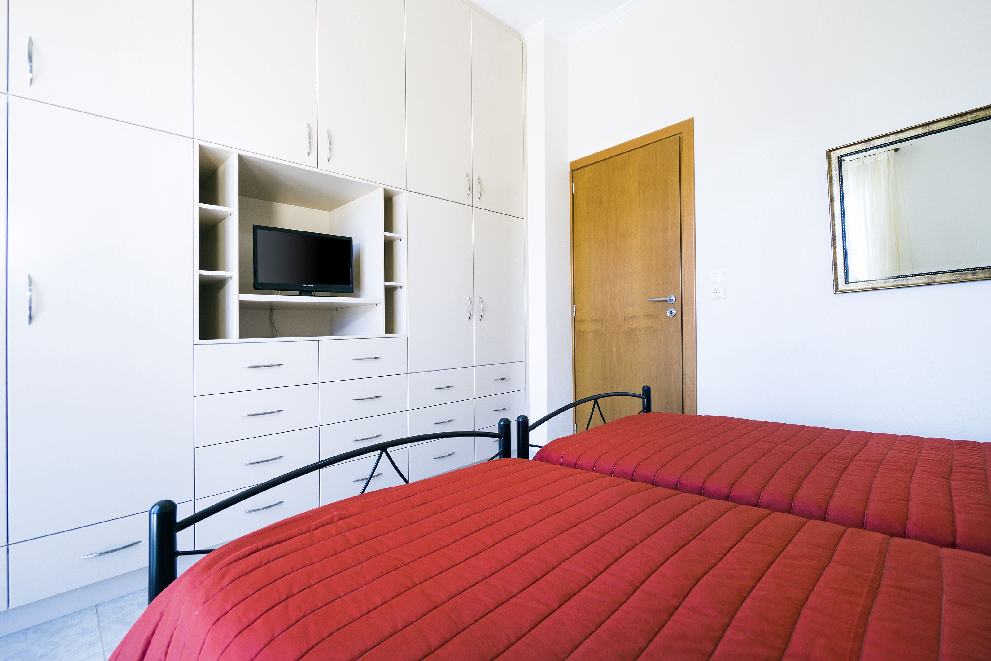 Un dormitorio con cama, televisor en un estante, armario y puerta.