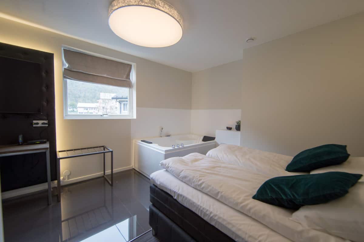 Een moderne slaapkamer met een groot bed, een ingebouwd bad en een raam met uitzicht op gebouwen.