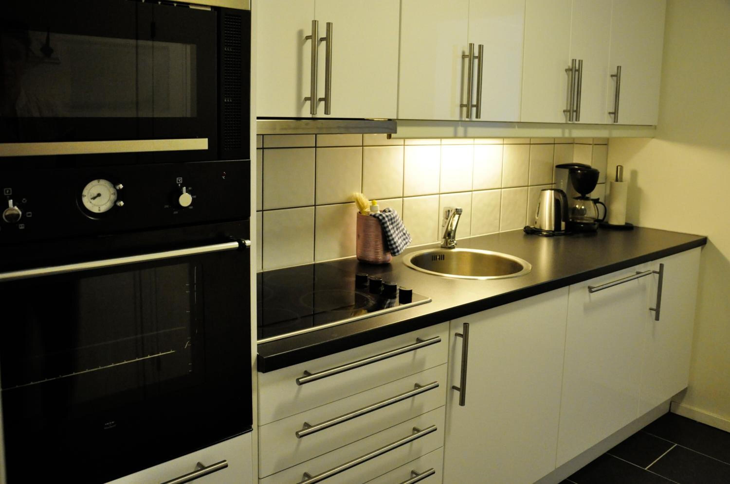 Uma cozinha moderna com eletrodomésticos de aço inoxidável, armários brancos e bancada preta.