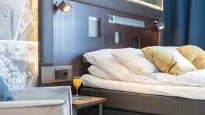 A hotel room with a bed, pillows, a bedside table with a glass of orange juice, and a small picture frame.