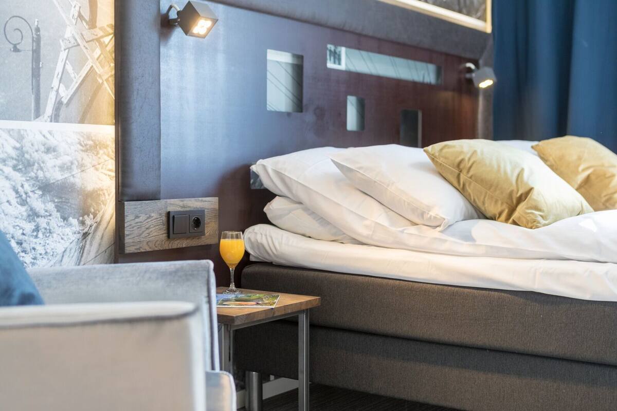 Een hotelkamer met een bed, kussens, een nachtkastje met een glas sinaasappelsap en een klein fotolijstje.