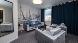 A modern hotel room with a grey sofa set, a round coffee table, and a large window with dark curtains.