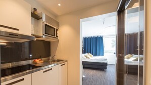 A modern kitchen with a microwave, oven, and sink, leading to a bedroom with a bed and a view of the outdoors.
