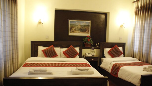 A hotel room with two beds, each with a red and white patterned bedspread, white pillows, and a small table with a magazine. - Hotel Peace N Park (Kathmandu)